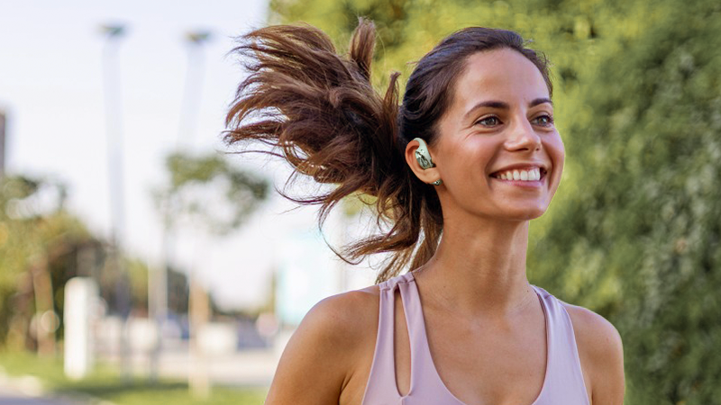 Lächelnde Frau beim Joggen mit Open-Ear-Kopfhörern – ideal für Sport und Bewegung im Freien.