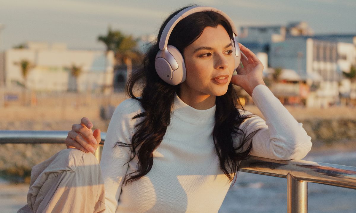 Frau mit Dual-Magnet-Treiber-Kopfhörern am Meer – klarer Sound, elegantes Design, perfekt für Musikgenuss unterwegs.