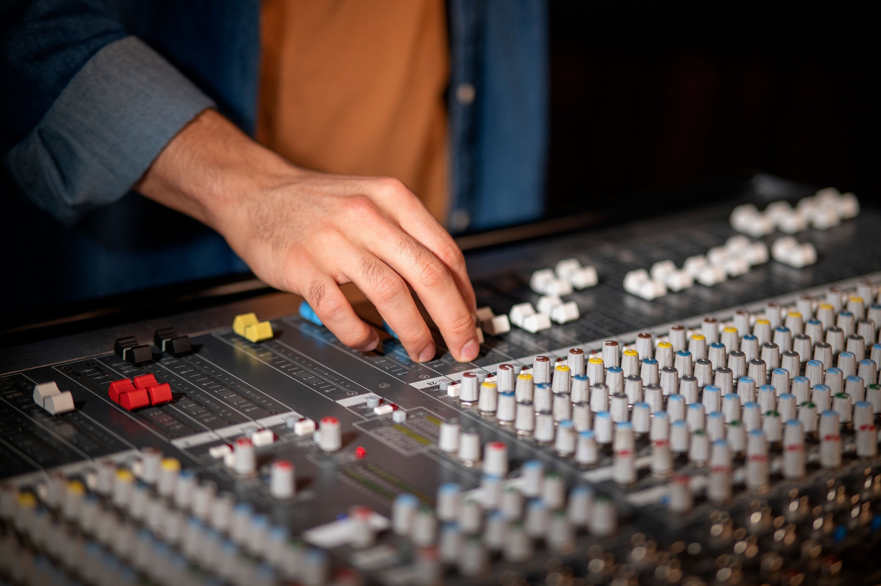 Hand stellt EQ-Regler an einem professionellen Audio-Mischpult für optimale Bluetooth-Kopfhörer-Klangqualität ein.