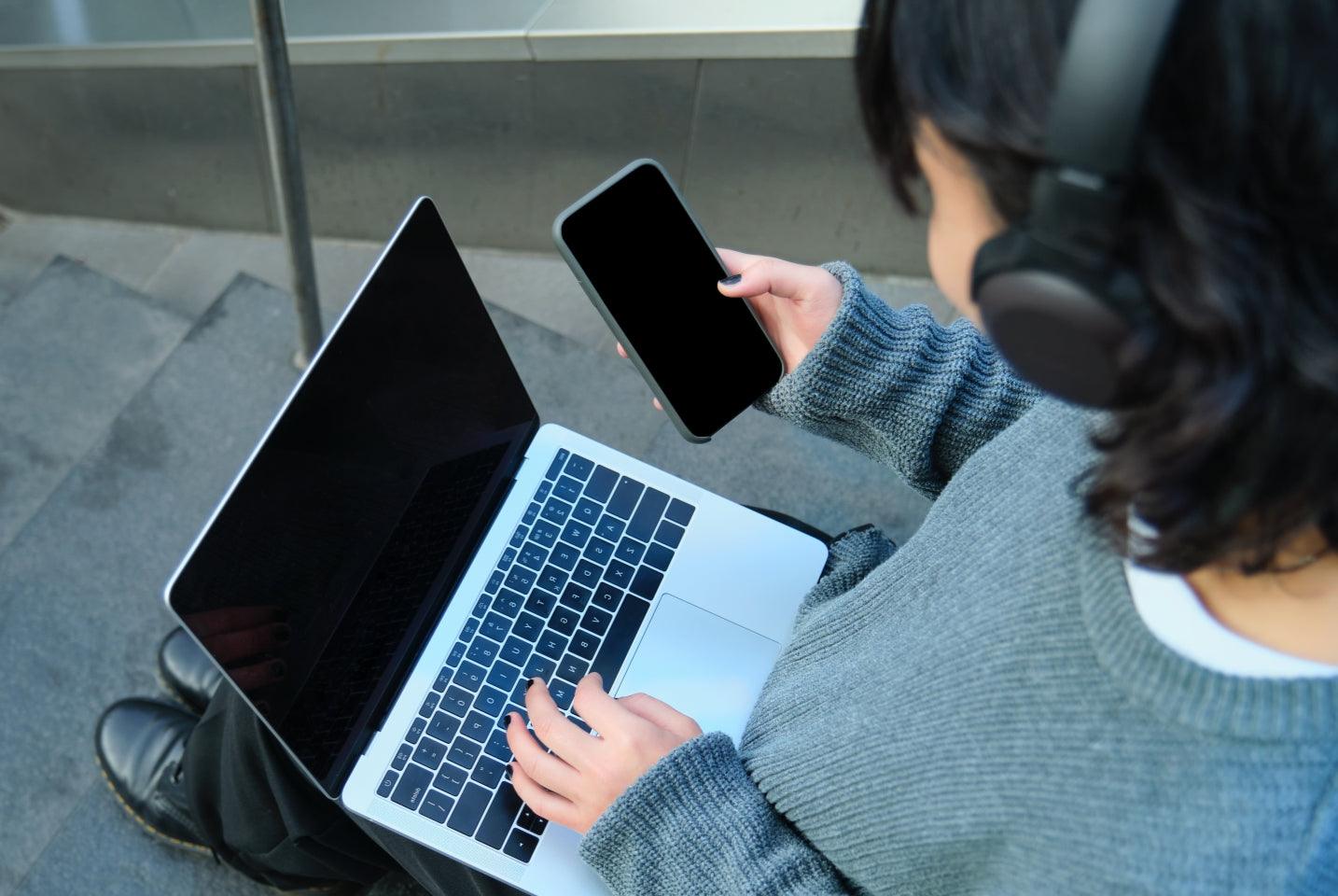 Frau mit Laptop und Smartphone nutzt Bluetooth-Ohrhörer – stabile Multi-Device-Verbindung im Alltag getestet.
