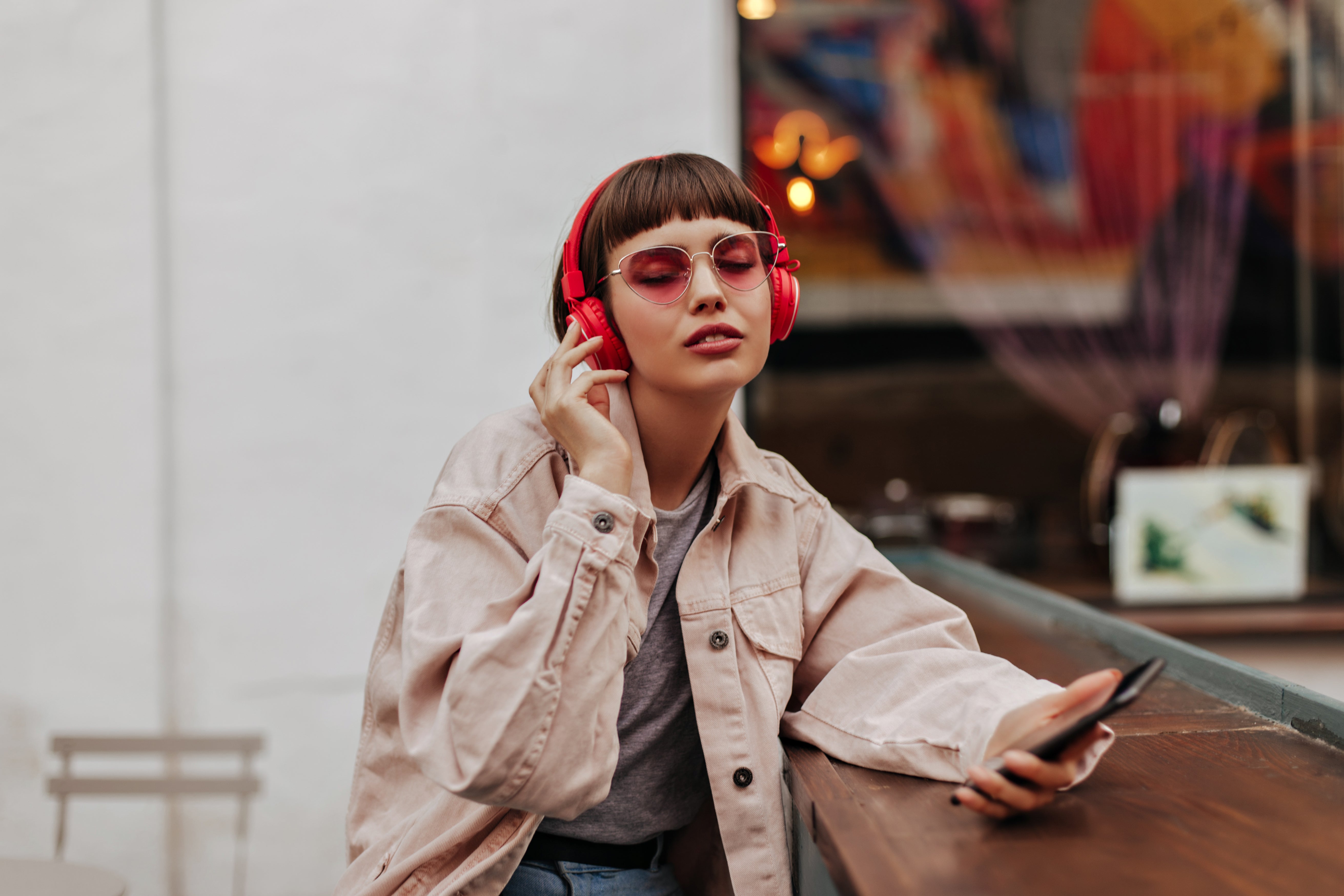 Frau mit roten kabellosen Kopfhörern und Sonnenbrille hört Musik im Café. Strahlung von Wireless-Kopfhörern?