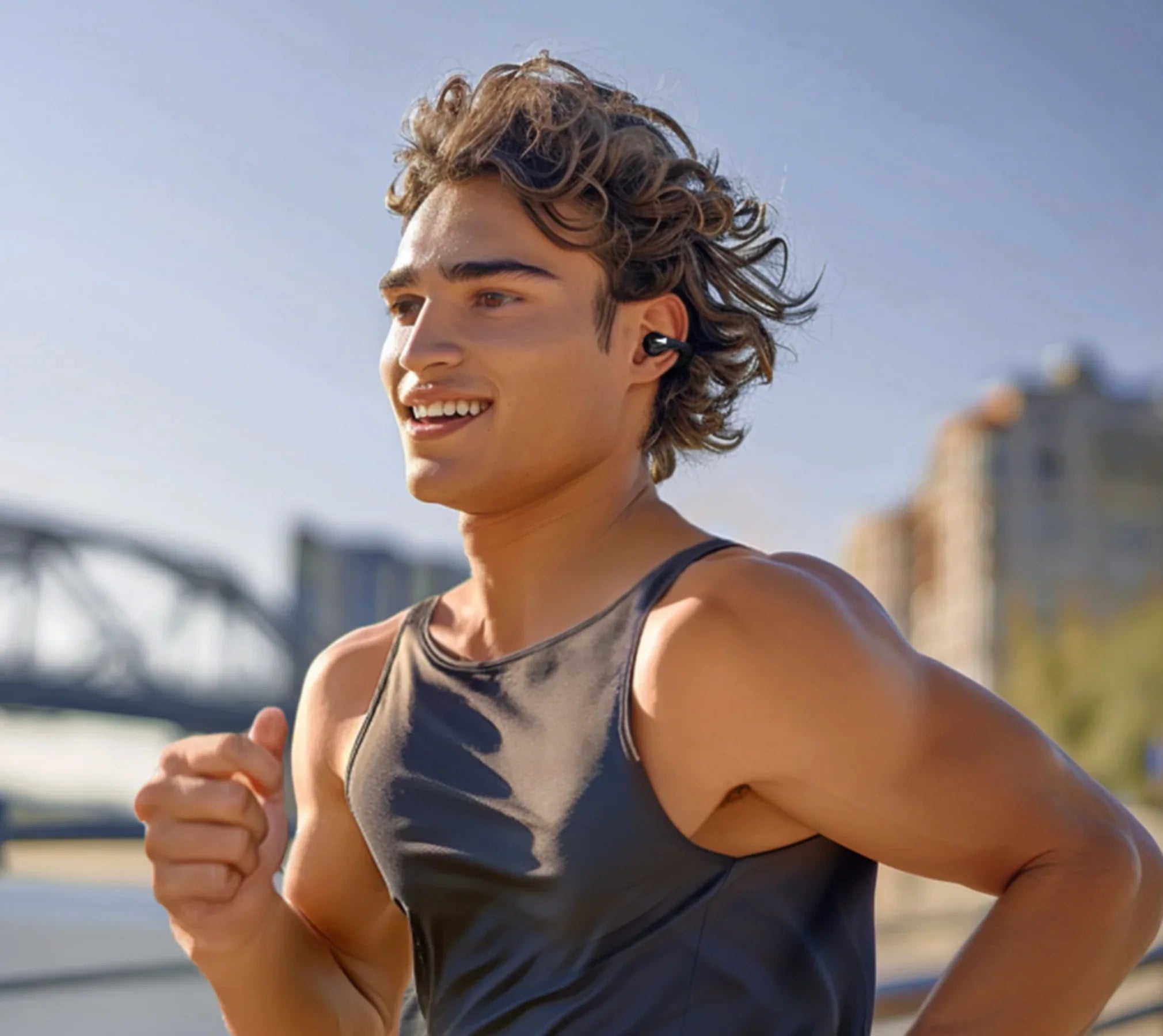 Jovem sorridente a correr com auscultadores sem fios, roupa de desporto ao ar livre