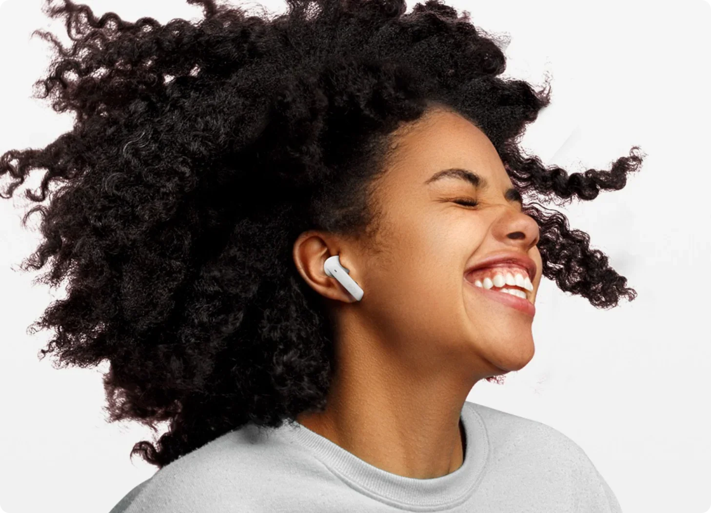 Mulher feliz com cabelo encaracolado e auscultadores intra-auriculares brancos.