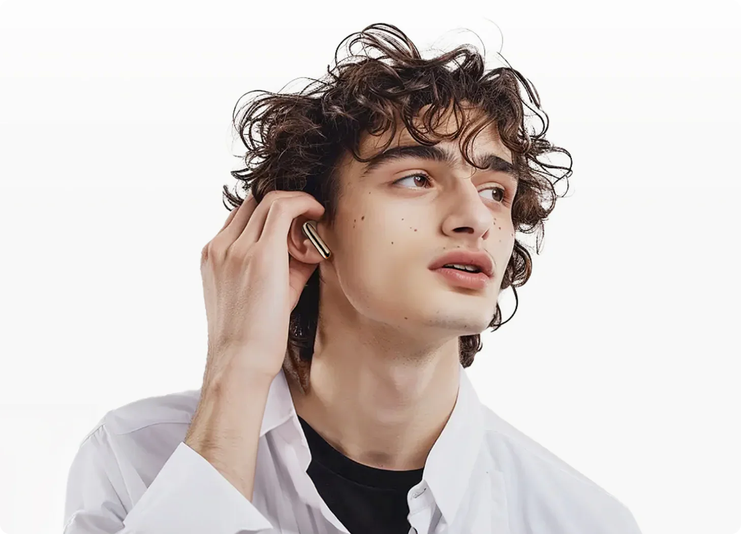 Jovem com cabelo encaracolado a colocar auscultadores sem fios dourados, camisa branca, estilo de vida moderno.