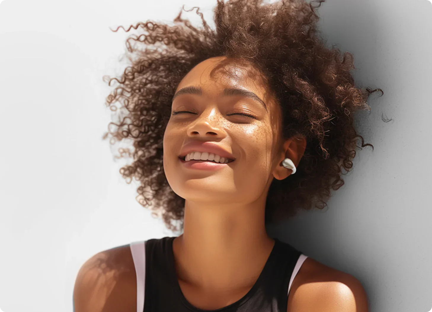 Mulher feliz com cabelo encaracolado e auscultadores brancos a desfrutar de música.