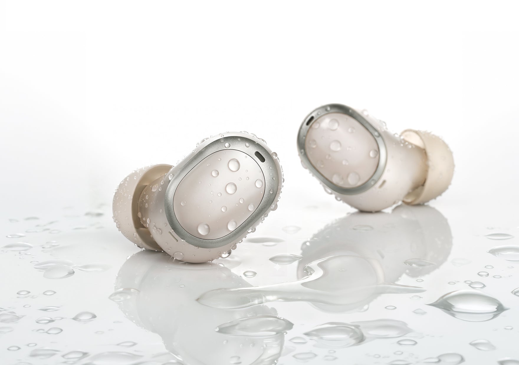 Auriculares intra-auriculares brancos impermeáveis com gotas de água numa superfície refletora.