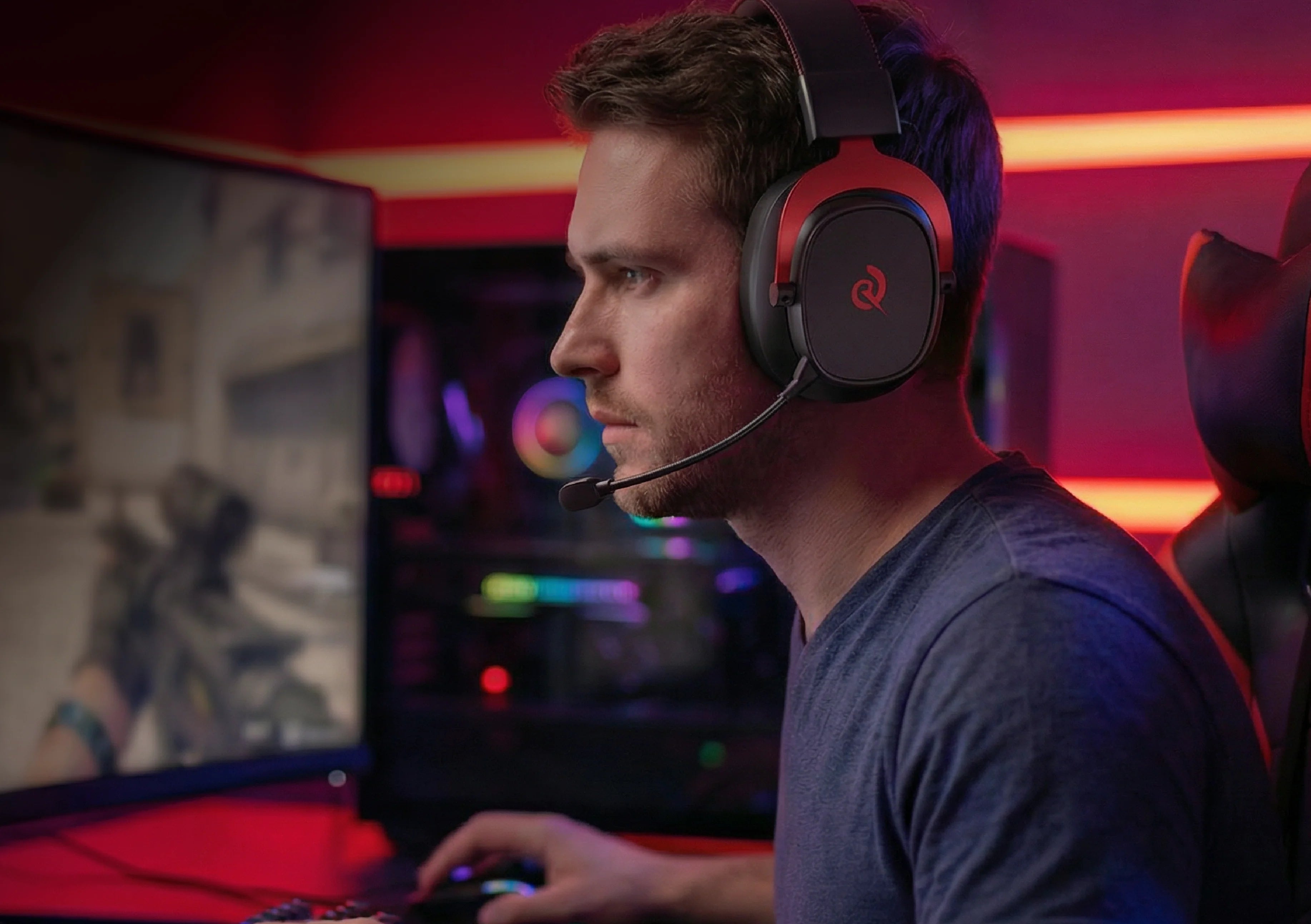 Homem com auscultadores de gaming e microfone em frente a monitor de PC, iluminação RGB brilhante ao fundo
